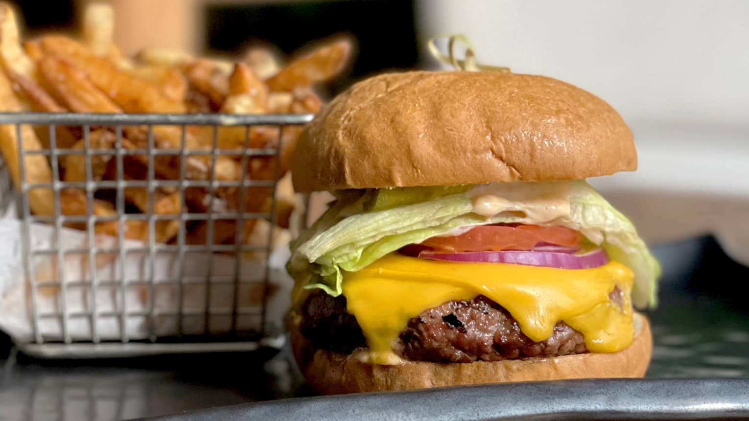 A burger with lettuce, tomato and cheese next to a small basket of fries.