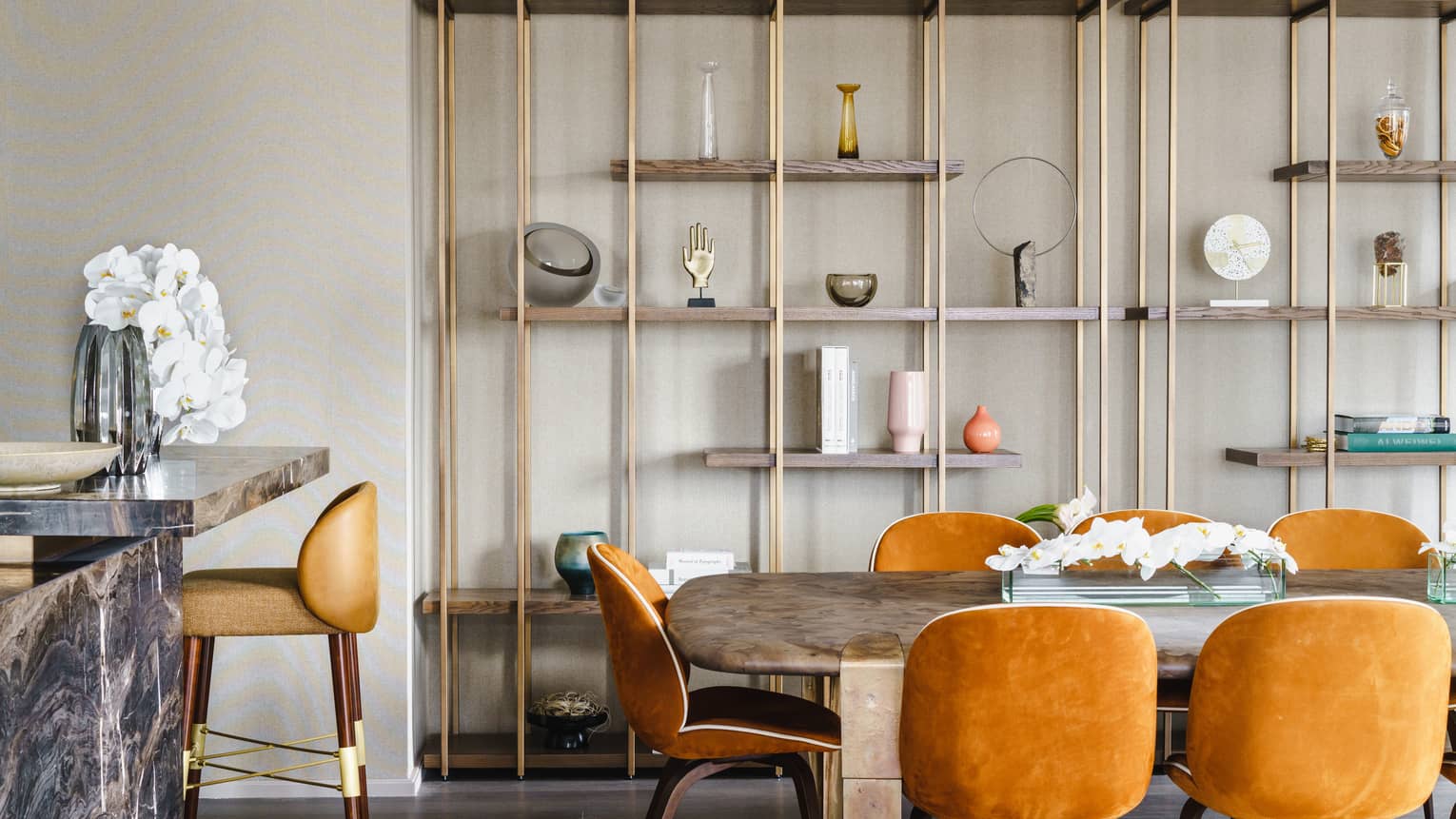 Dining table with orange velvet chairs, modern shelving on the wall, bar with high-top chair
