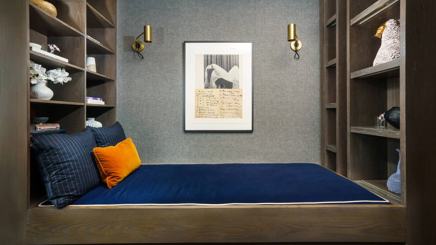 Cozy reading nook with naby blue daybed, orange accent pillow, framed art, and built-in shelves with decor and books