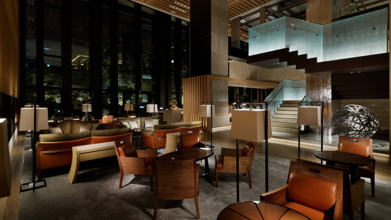 Brasserie dimly-lit dining room, brown leather chairs, tables, sofas under glass staircase
