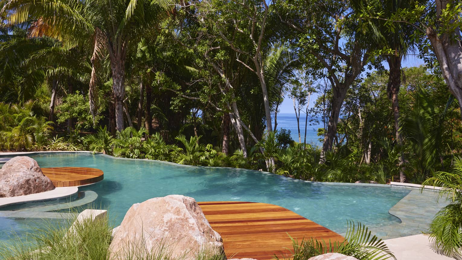 Pool surrounded by tropical forest, with the ocean visible through the trees