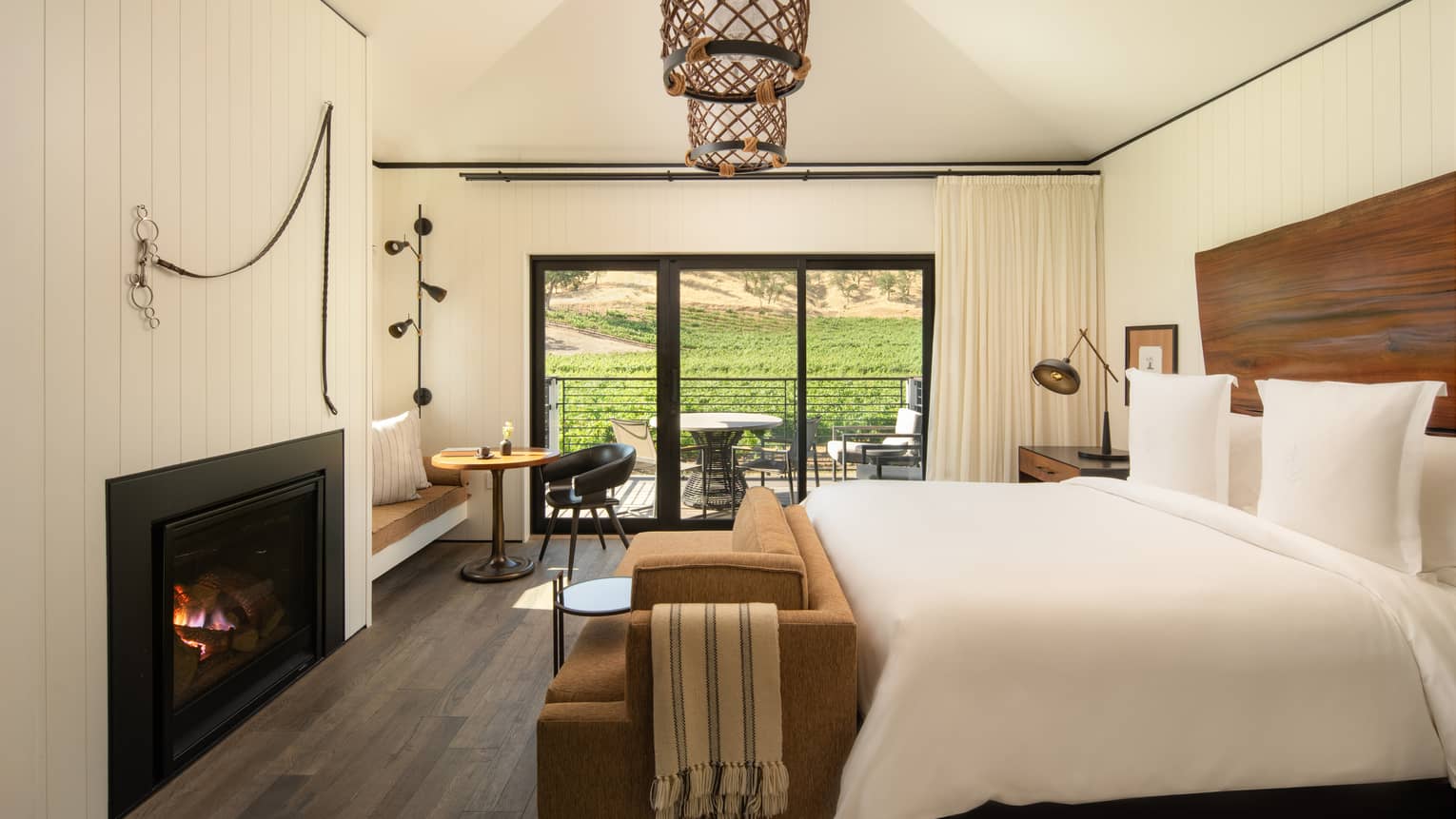 Contemporary bedroom of a resort suite, featuring king bed, fireplace, natural wood headboard, two hanging lights and walk-out terrace