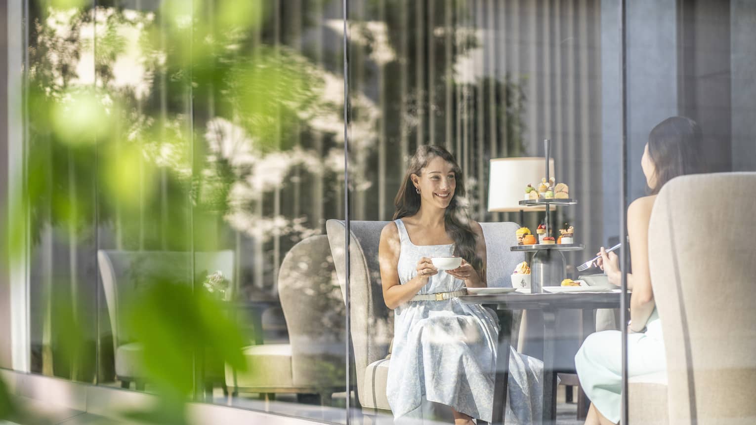 View through cafe glass window where two women enjoy afternoon tea and desserts
