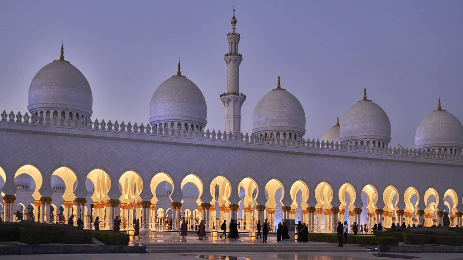 Stunning white marble mosque at dusk features a minaret with pointed domes at either side; keyhole arches line the entrance.
