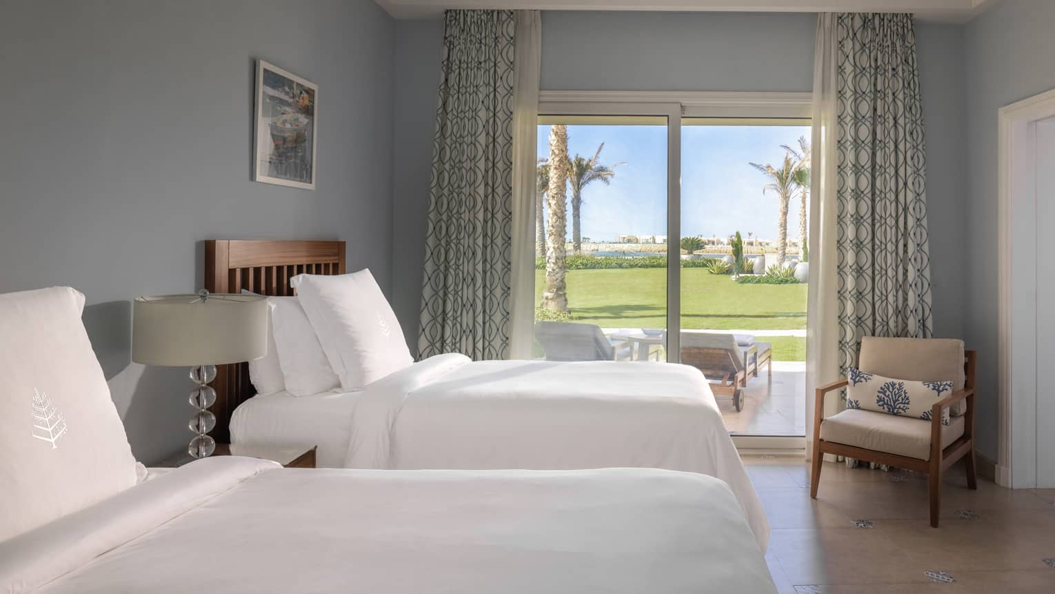 Guest room with twin beds and white linens, tan armchair in corner, sliding glass door to patio