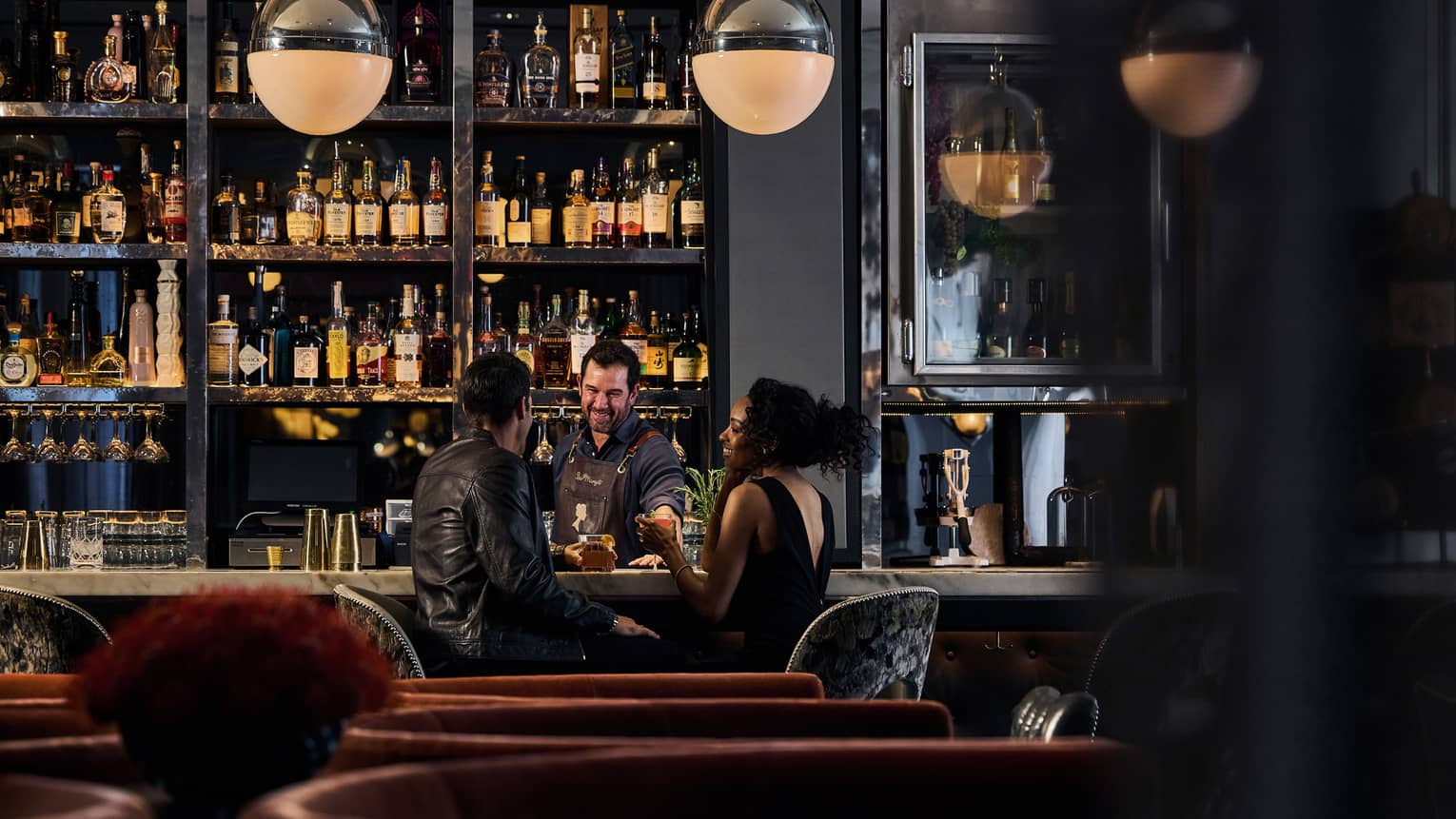 A bartender smiles as he serves a couple sitting at a modern, spacious bar