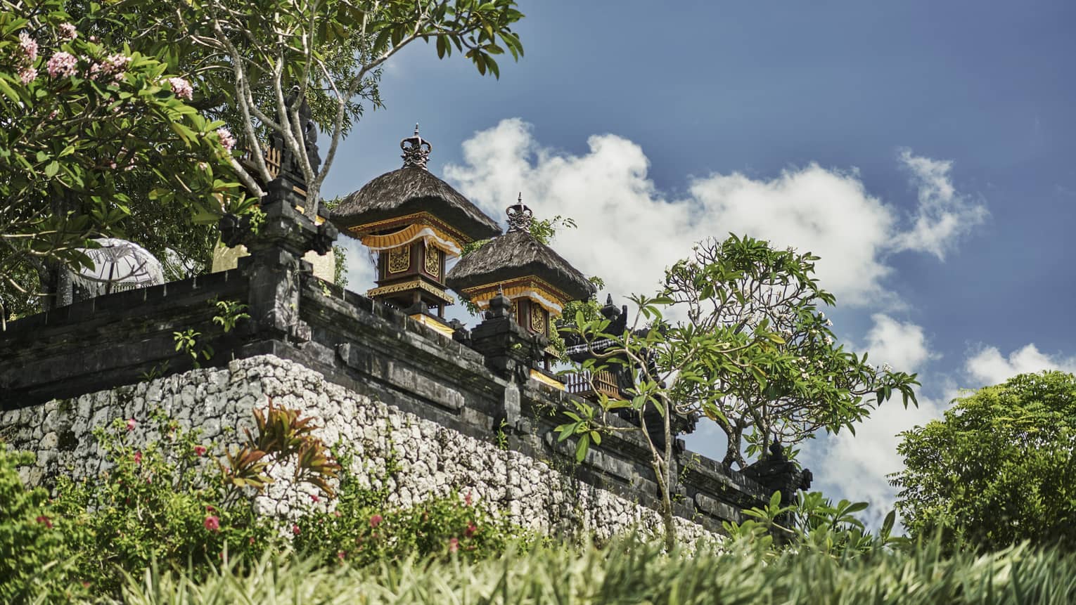 Exterior view of resort temple with stone wall, posts and carvings, tropical trees