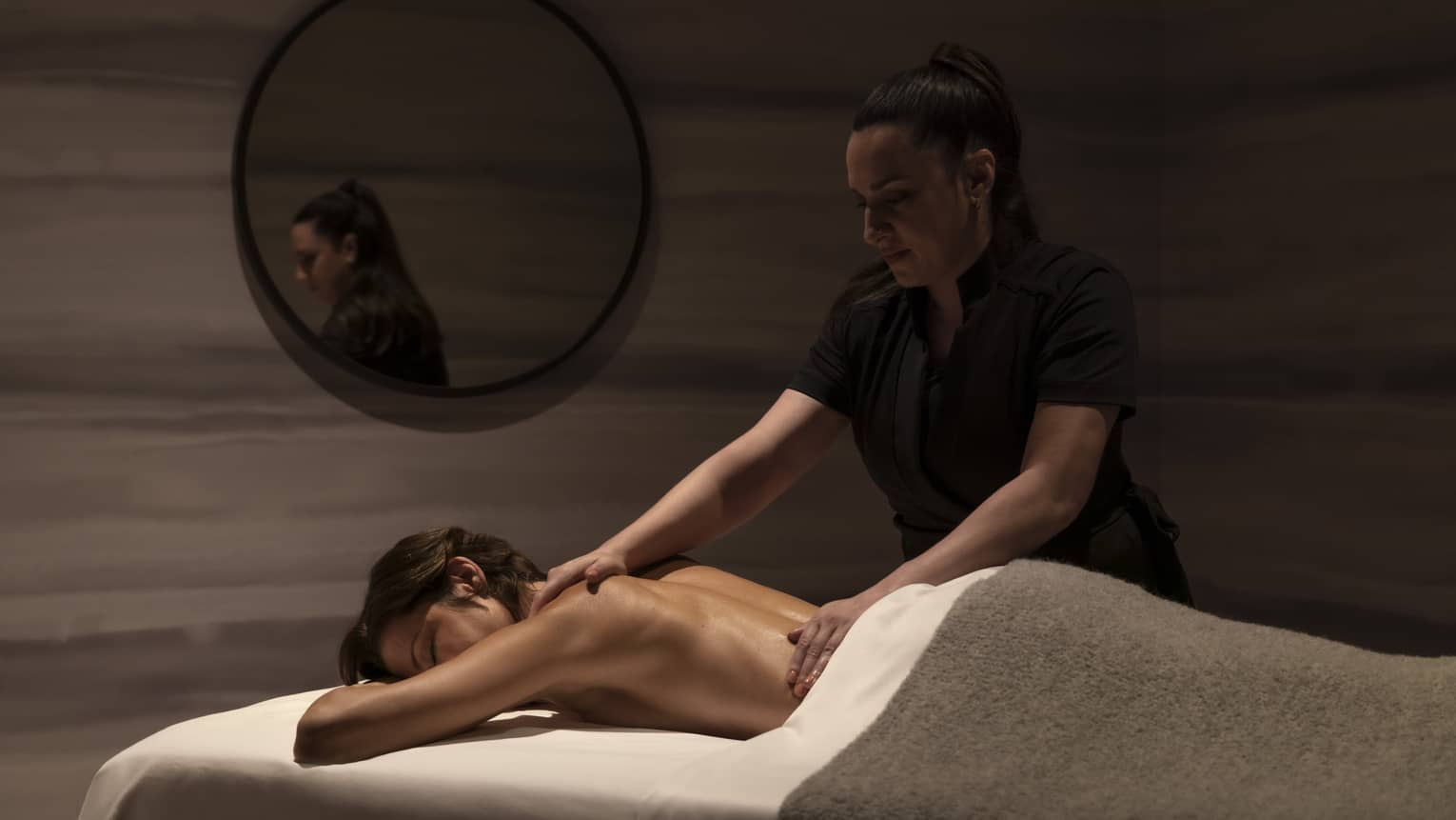 A spa staff member massaging a woman in a dimly lit room.