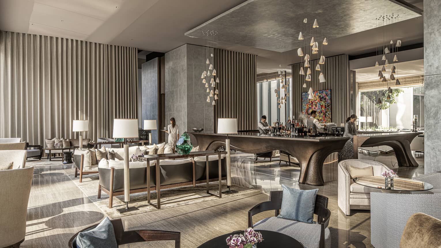 Lounge area with armchairs, sofas and tables, four abstract lighting fixtures hang from ceiling
