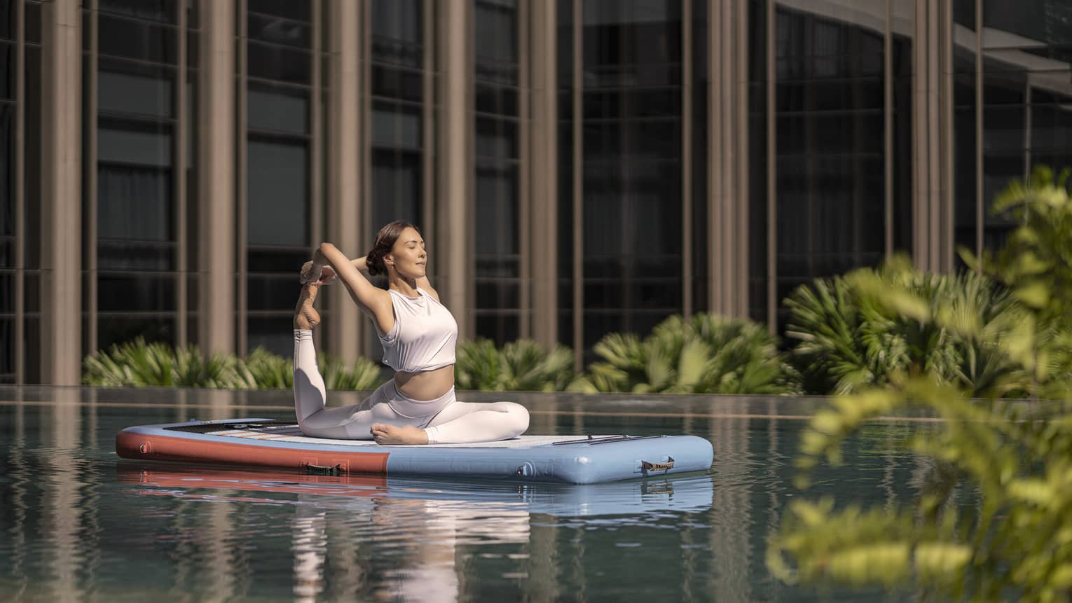 Woman doing a yoga pose on a floating paddle board in hotel pool