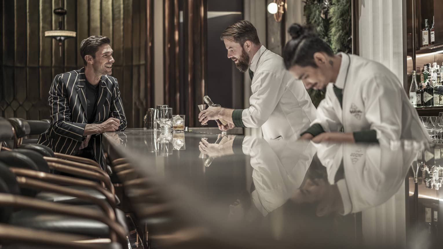 BKK Social Club, row of stools to where bartenders prepare drink for smiling man wearing striped suit