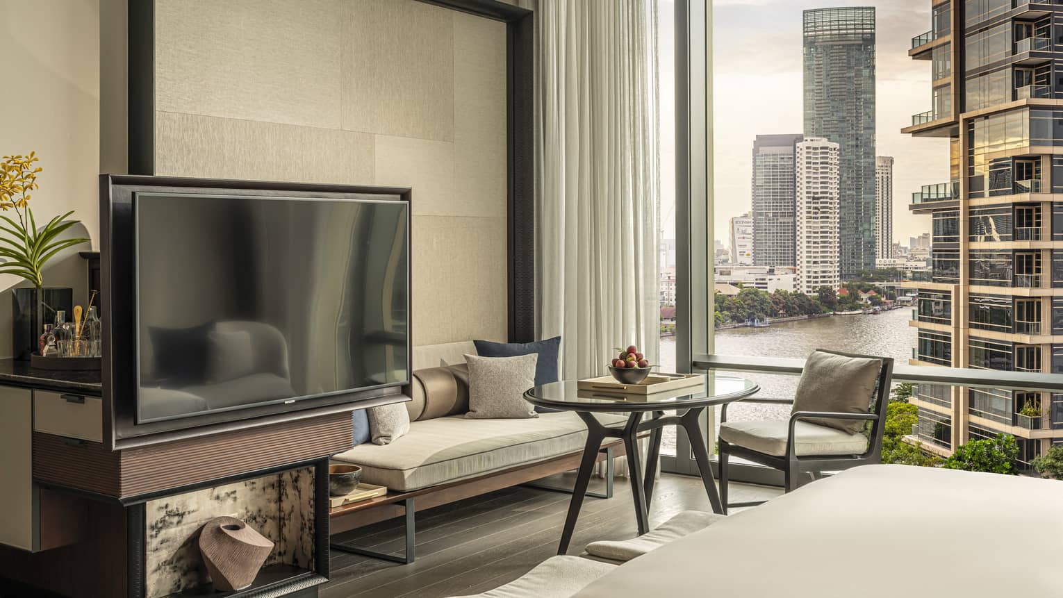 Hotel room with TV, sofa, chair and table with window wall
