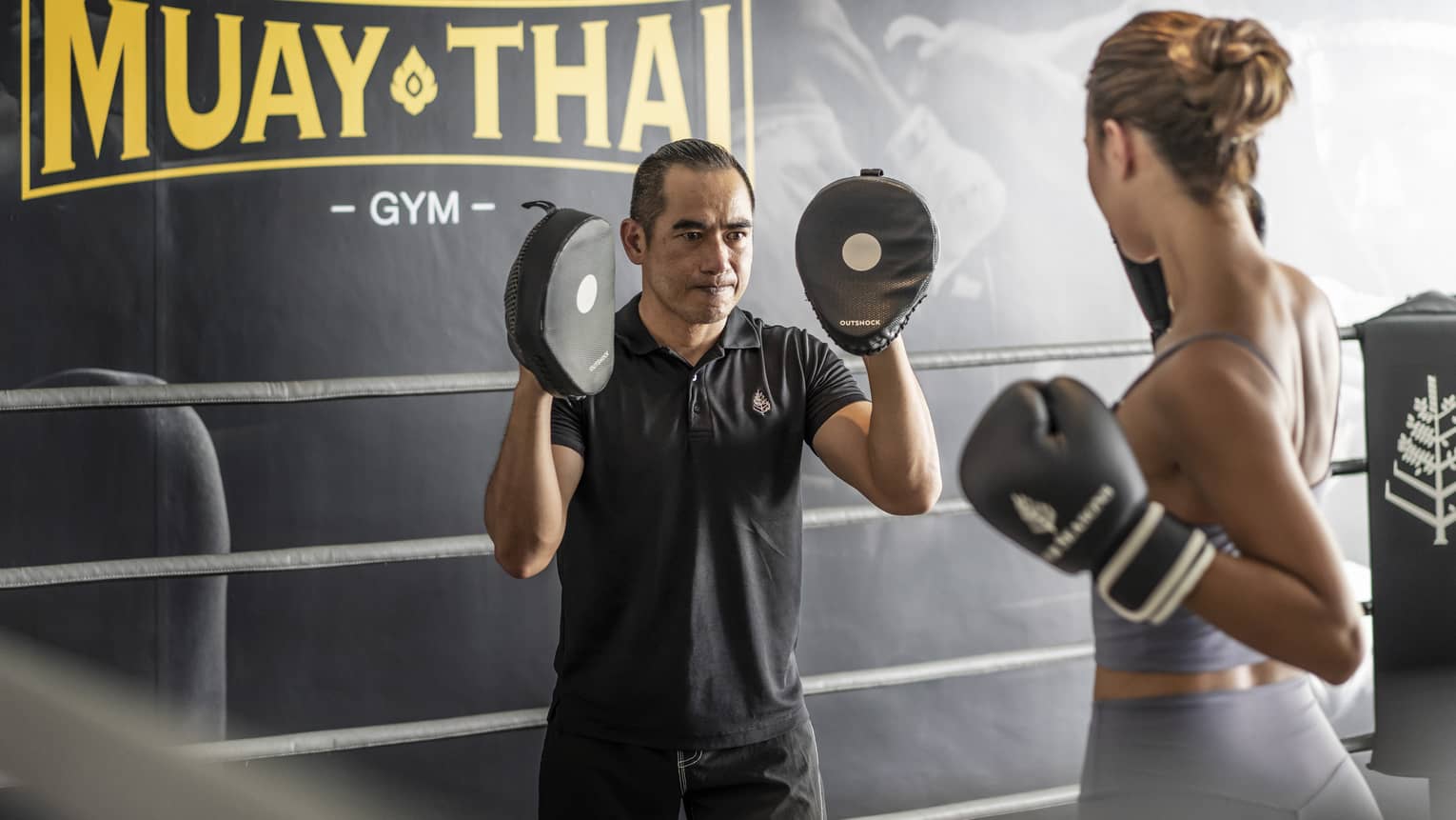 Woman practices Muay Thai with instructor in the ring of a gym