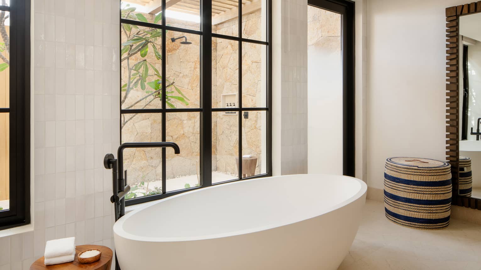 Luxury resort bathroom with standalone oval tub next to an outdoor shower window