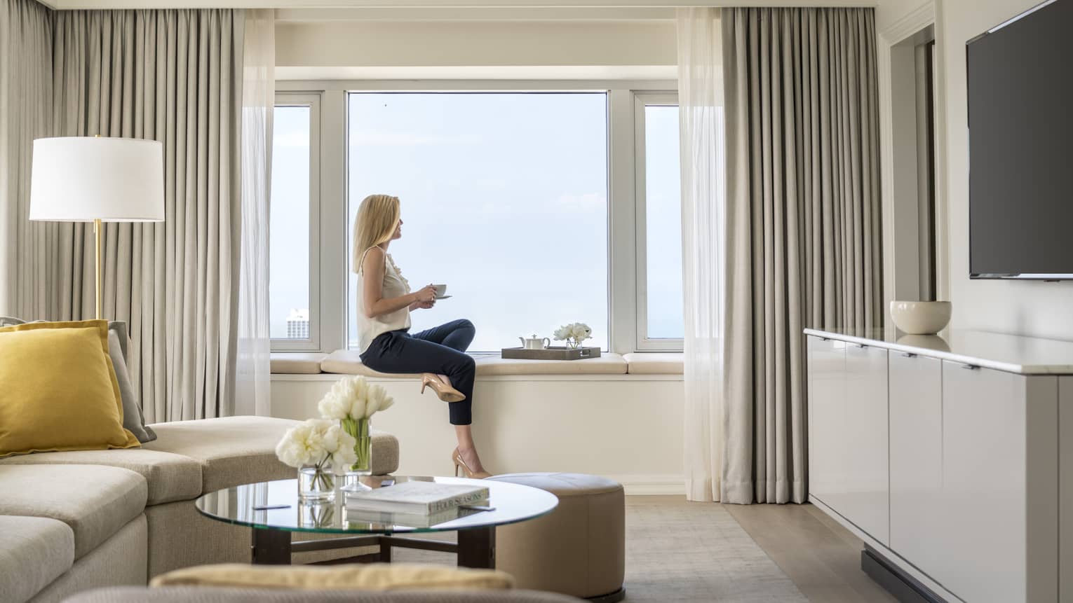A woman hold a cup of tea and sits on a windowsill in a One Bedroom Suite