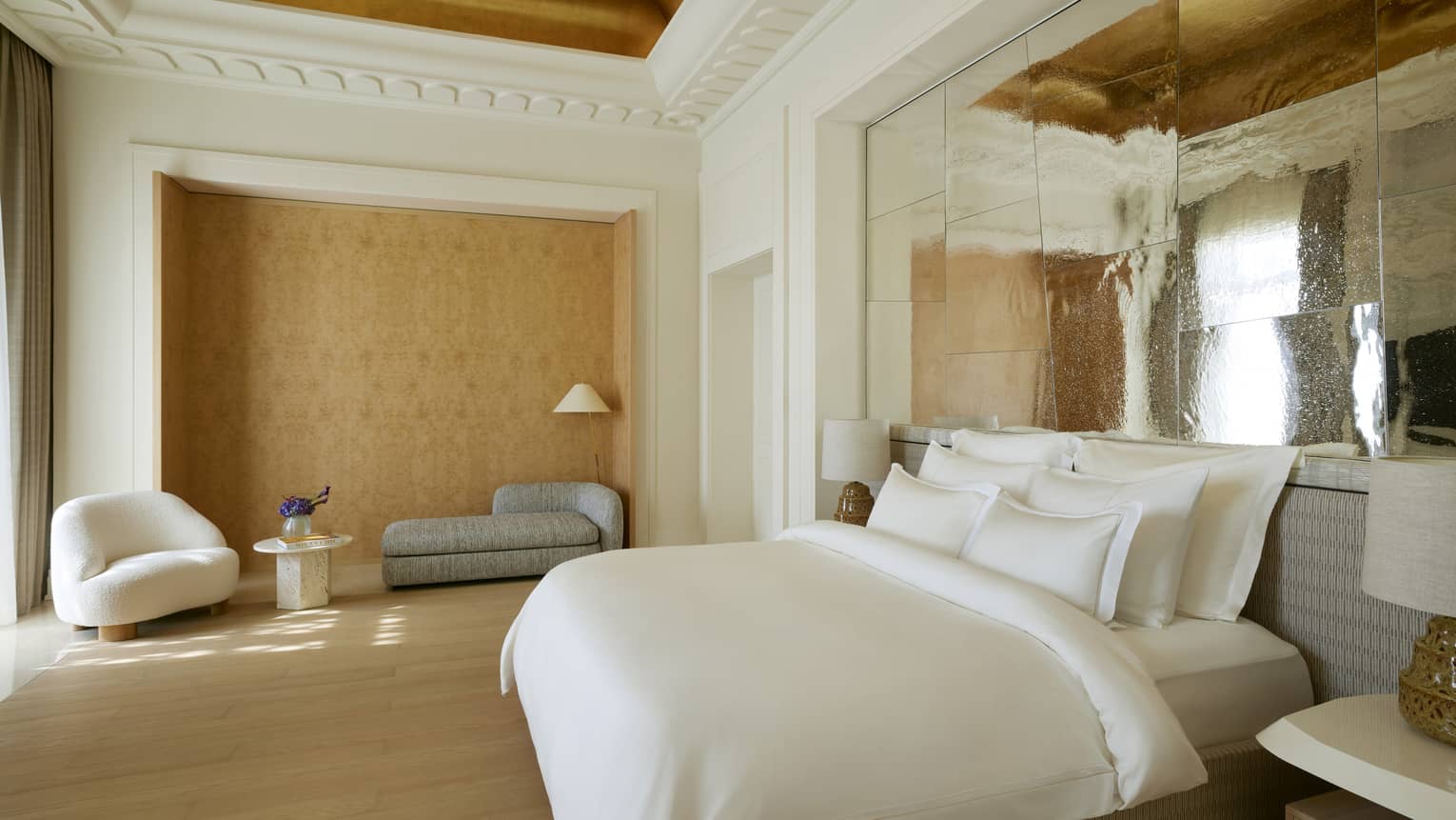 Primary bedroom of a luxury hotel suite, with king bed under an intricate painting ceiling with crown molding
