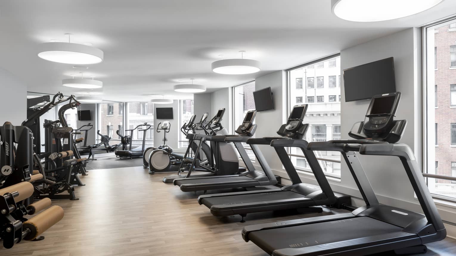Fitness room with three treadmills, bikes and weight-training equipment, lined with windows