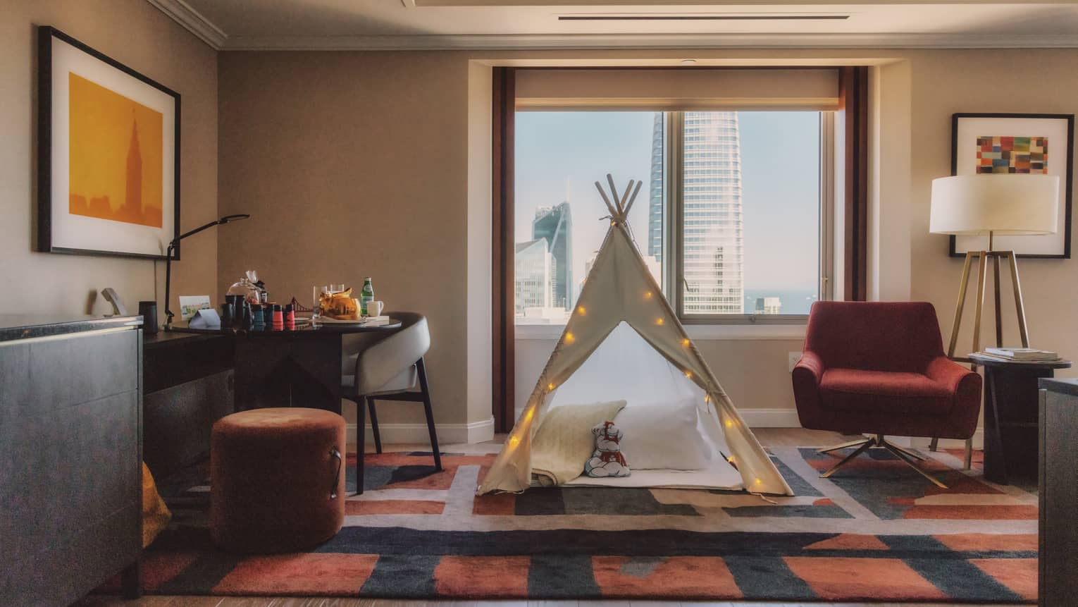 A child's triangular play tent with fairy lights sits in front of a large window in a guest room.