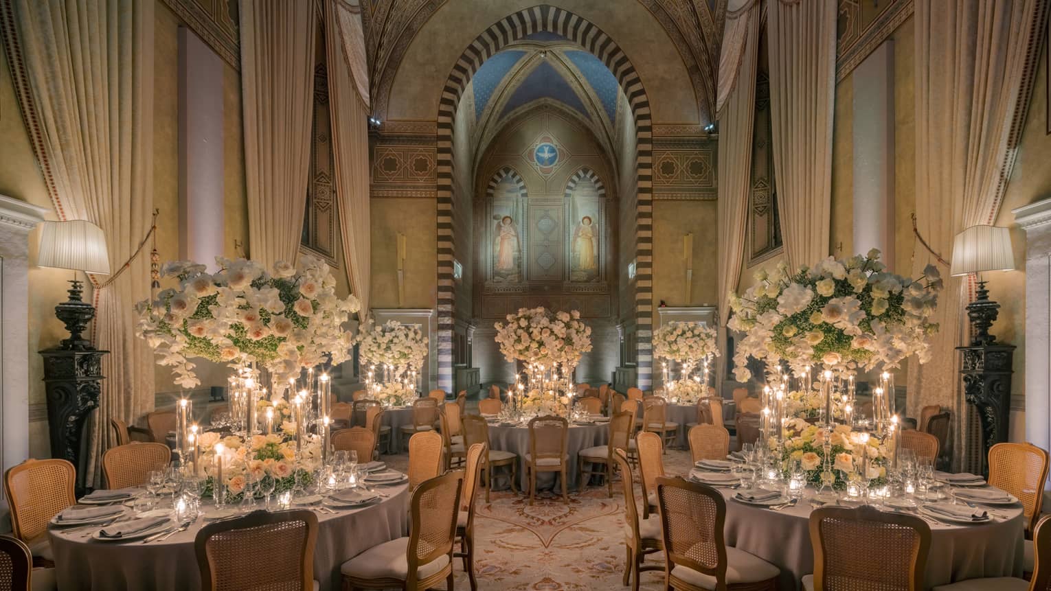 Grand dining room with tall arched ceilings and round elegantly set tables with tall white flower centrepieces