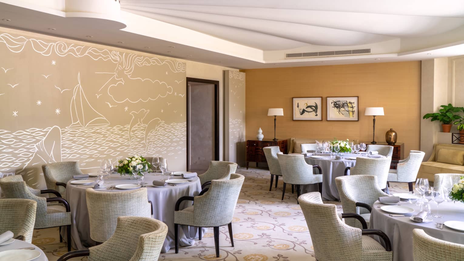 Le Cap restaurant, round set tables, beige rounded chairs, beige sea-themed wall mural
