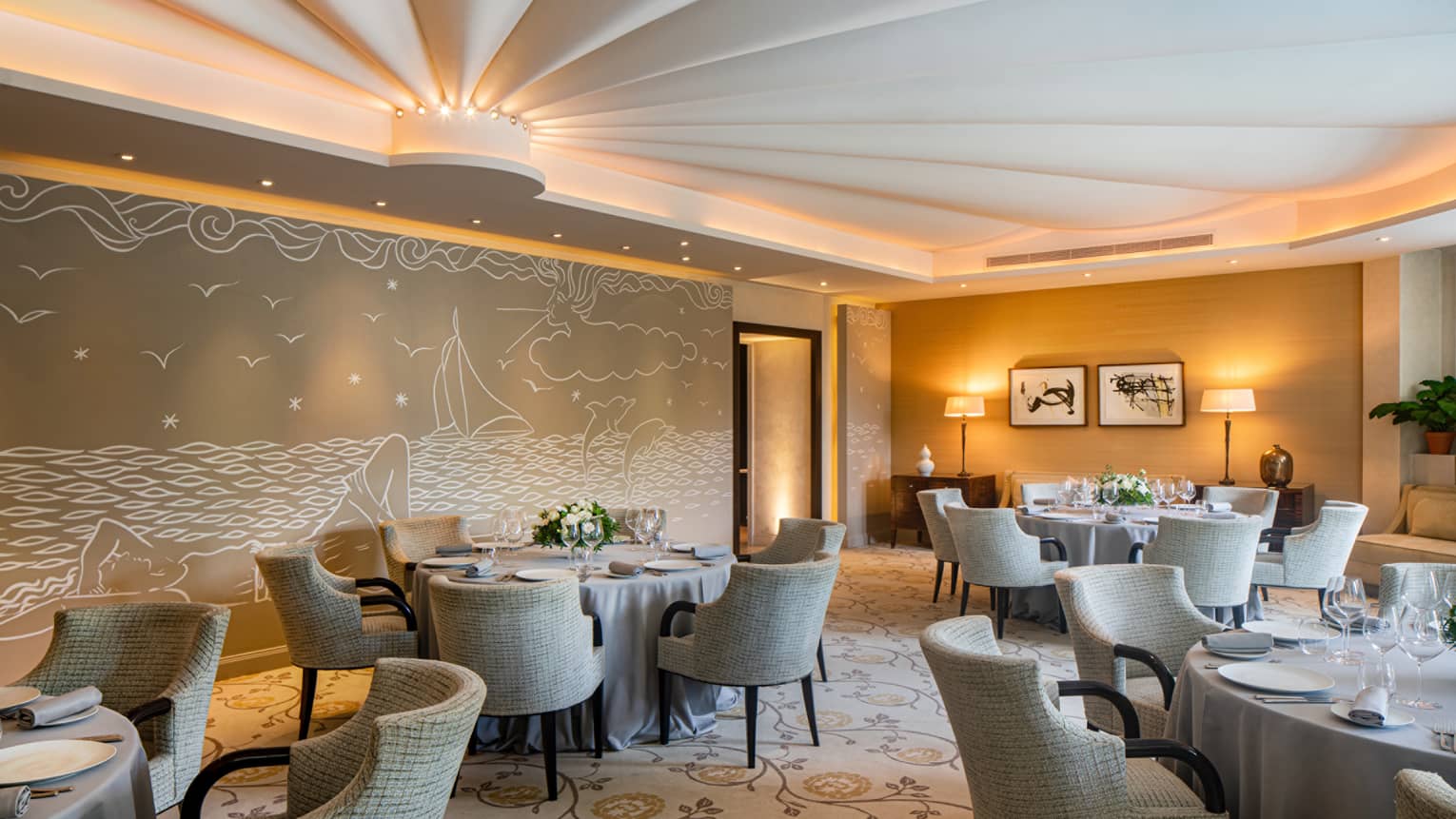 Le Cap restaurant, round set tables, beige rounded chairs, beige sea-themed wall mural, uplit ceiling