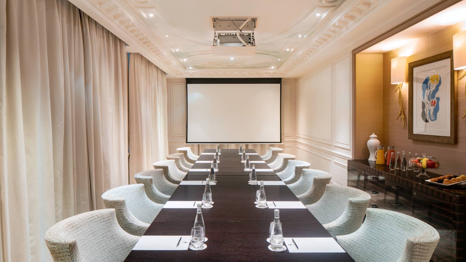 Long, narrow meeting room with conference table and beige chairs, curtained window to left, rear screen