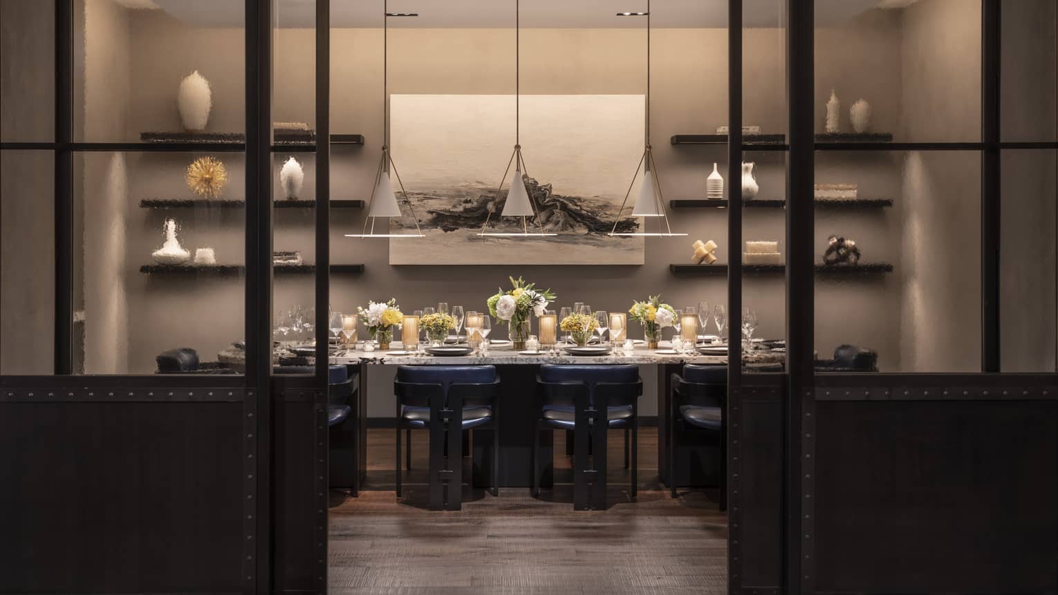 A private dining room with a large table covered in flowers and a painting and shelves on a wall.