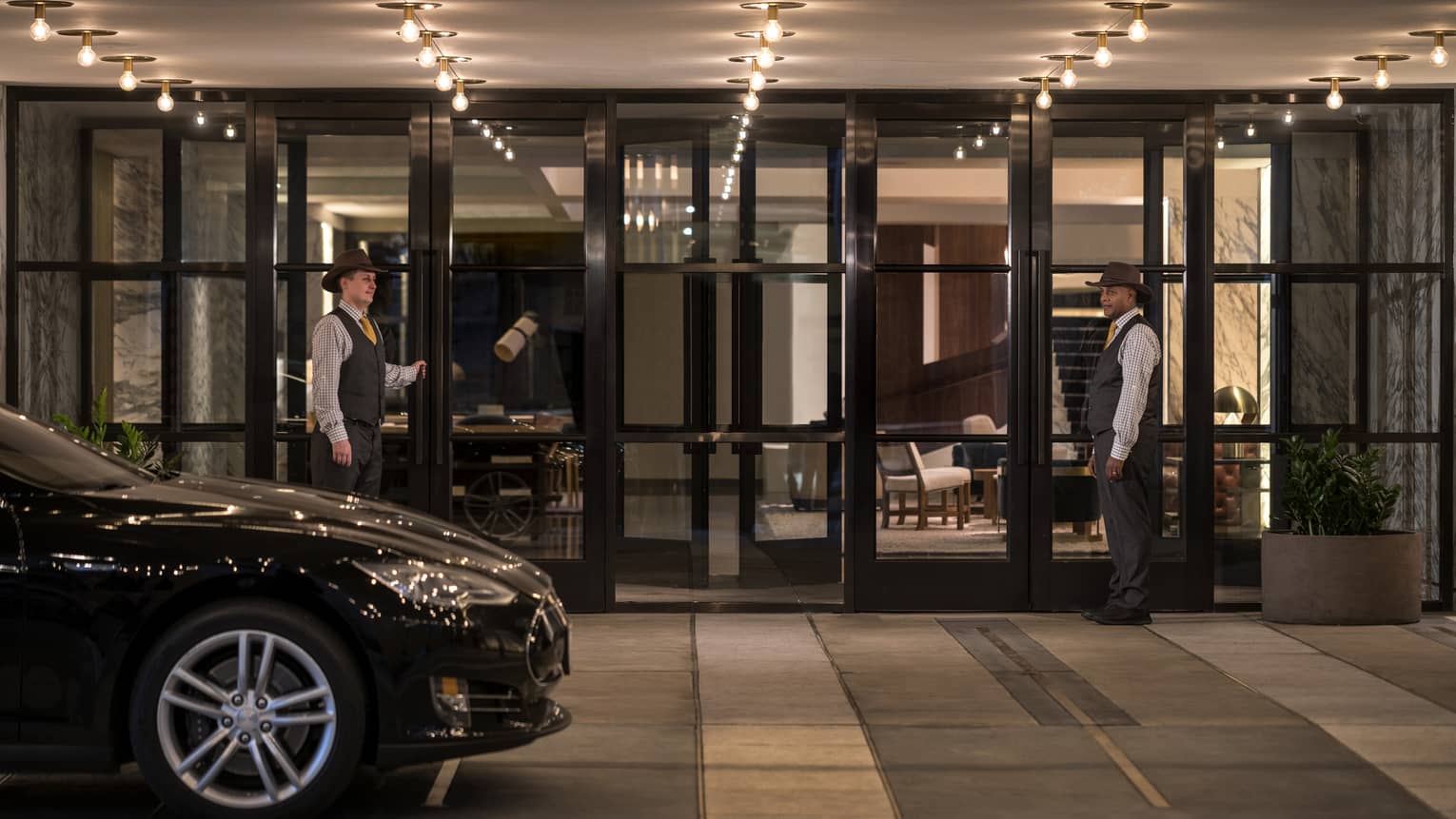 A car pulling up to the valet entrance of a hotel with two team members standing by glass doors.