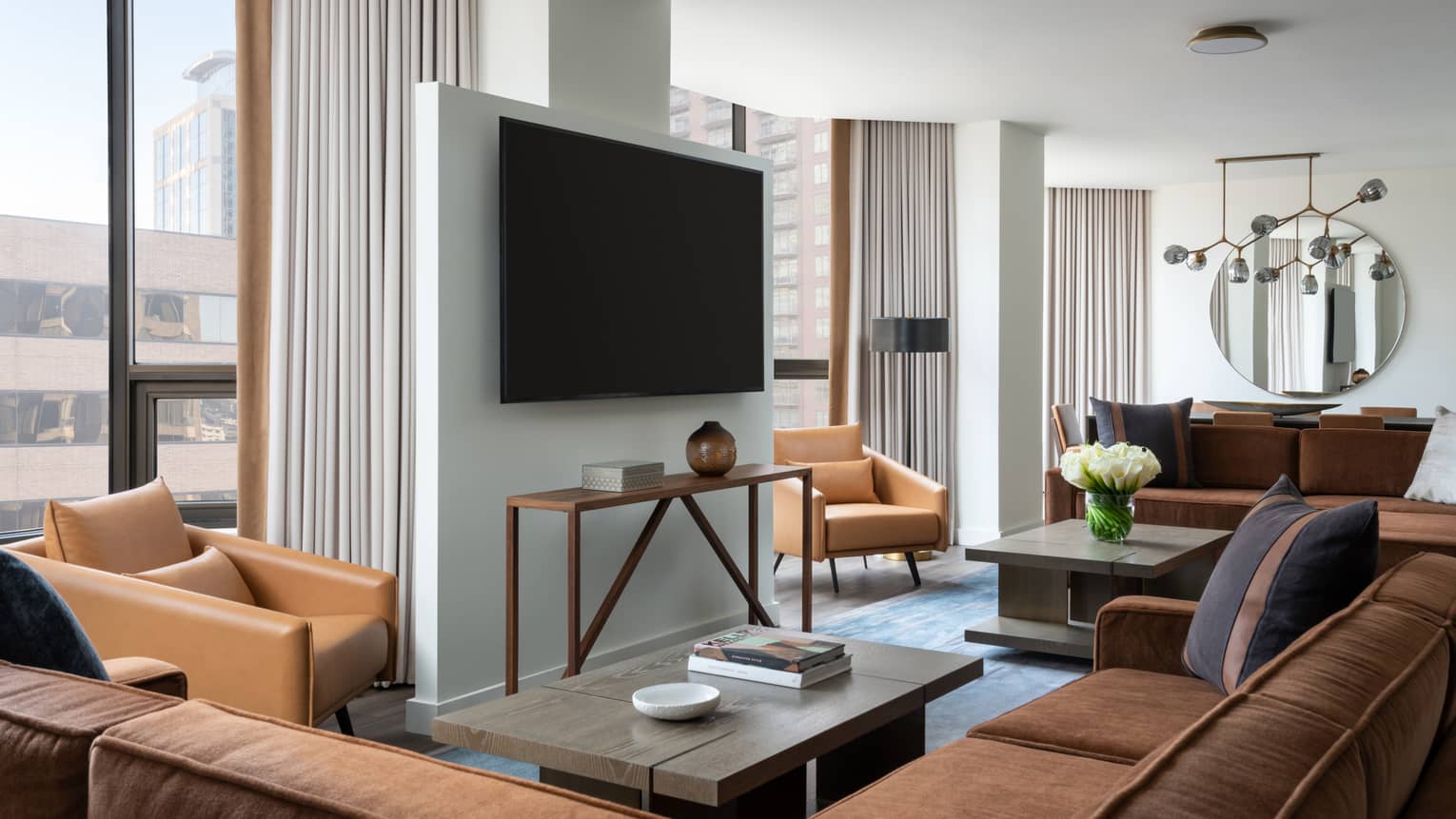 Living room with brown suede sectional sofa, light brown leather arm chairs, coffee table, hanging TV, windows