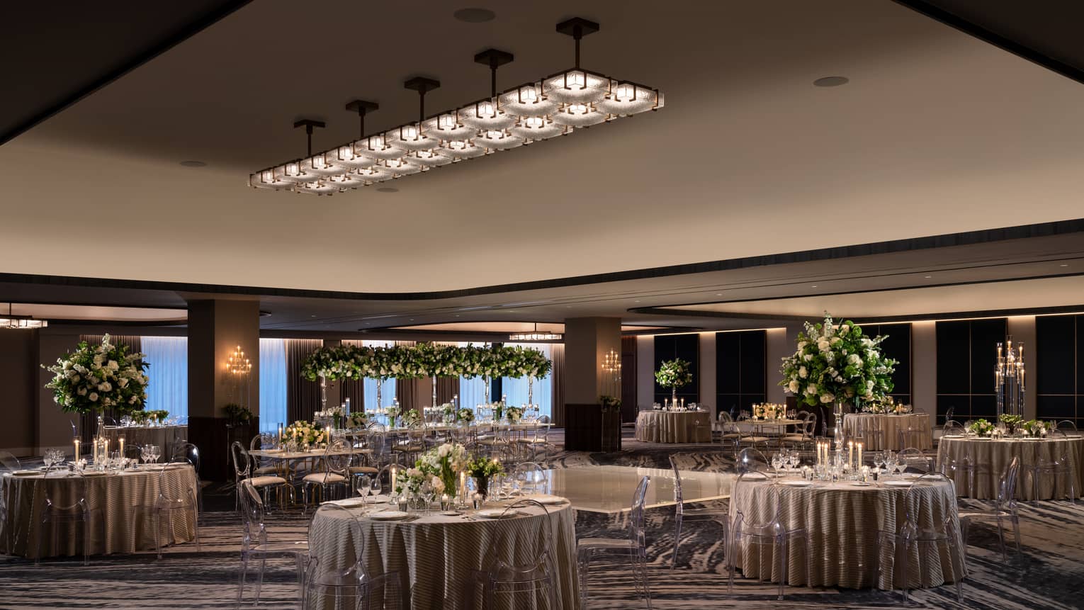A ballroom with round tables and grey table clothes with flowers and plants as centerpieces on the tables.