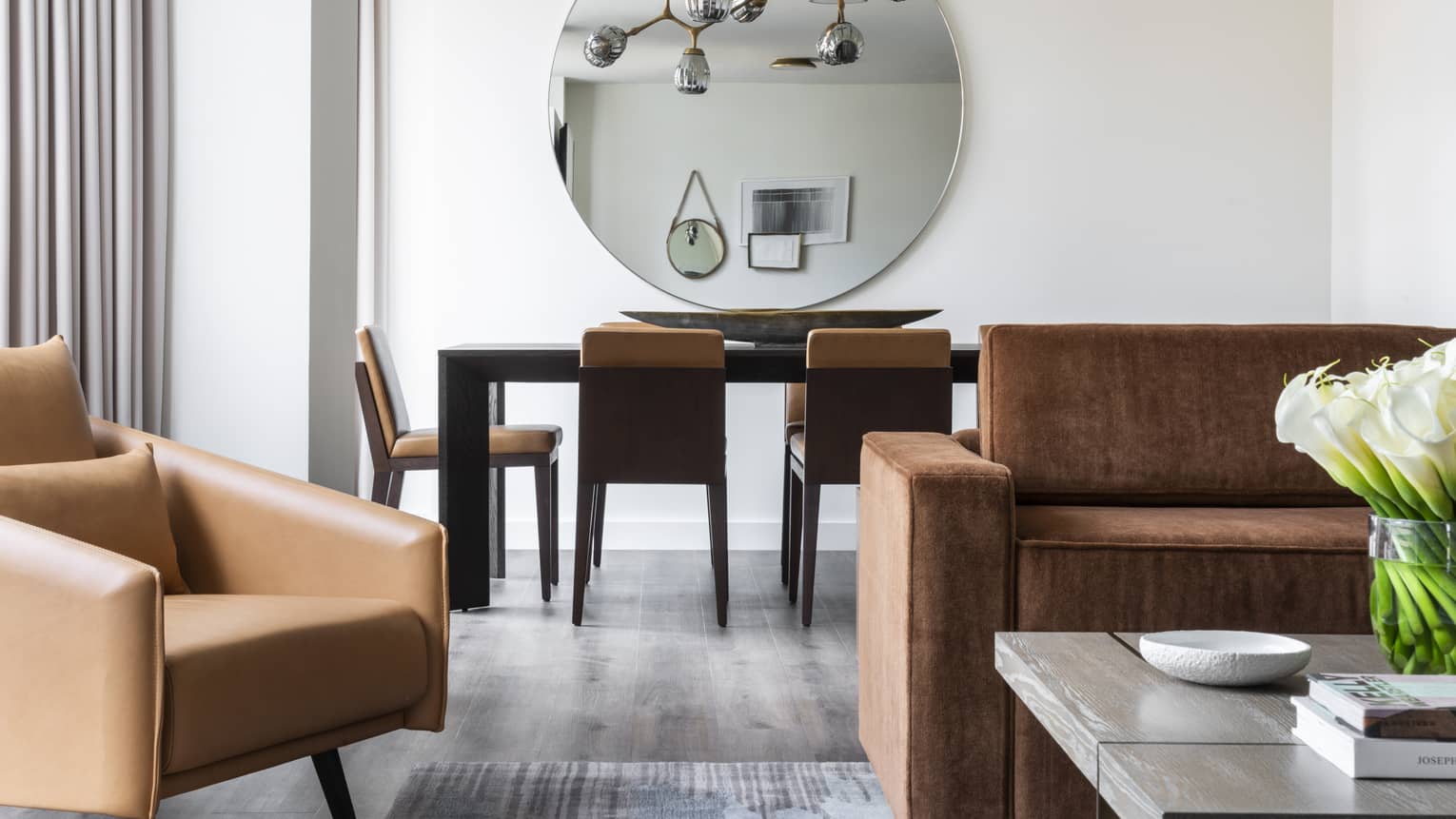 A living and dining room with a leather chair and sofa, a coffee table, and a dining table with chairs around it.