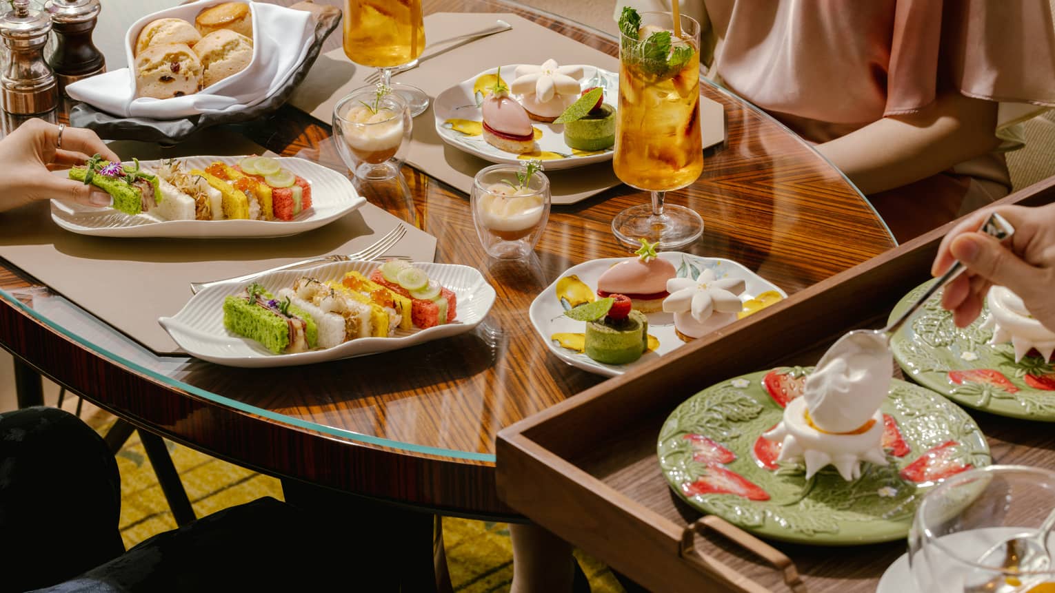 A wooden dining table scattered with afternoon tea dishes and drinks