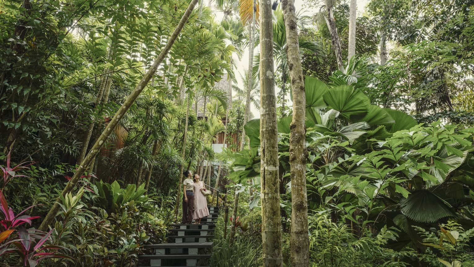 Female spa staff and guest walk along tree-lined pathway to spa
