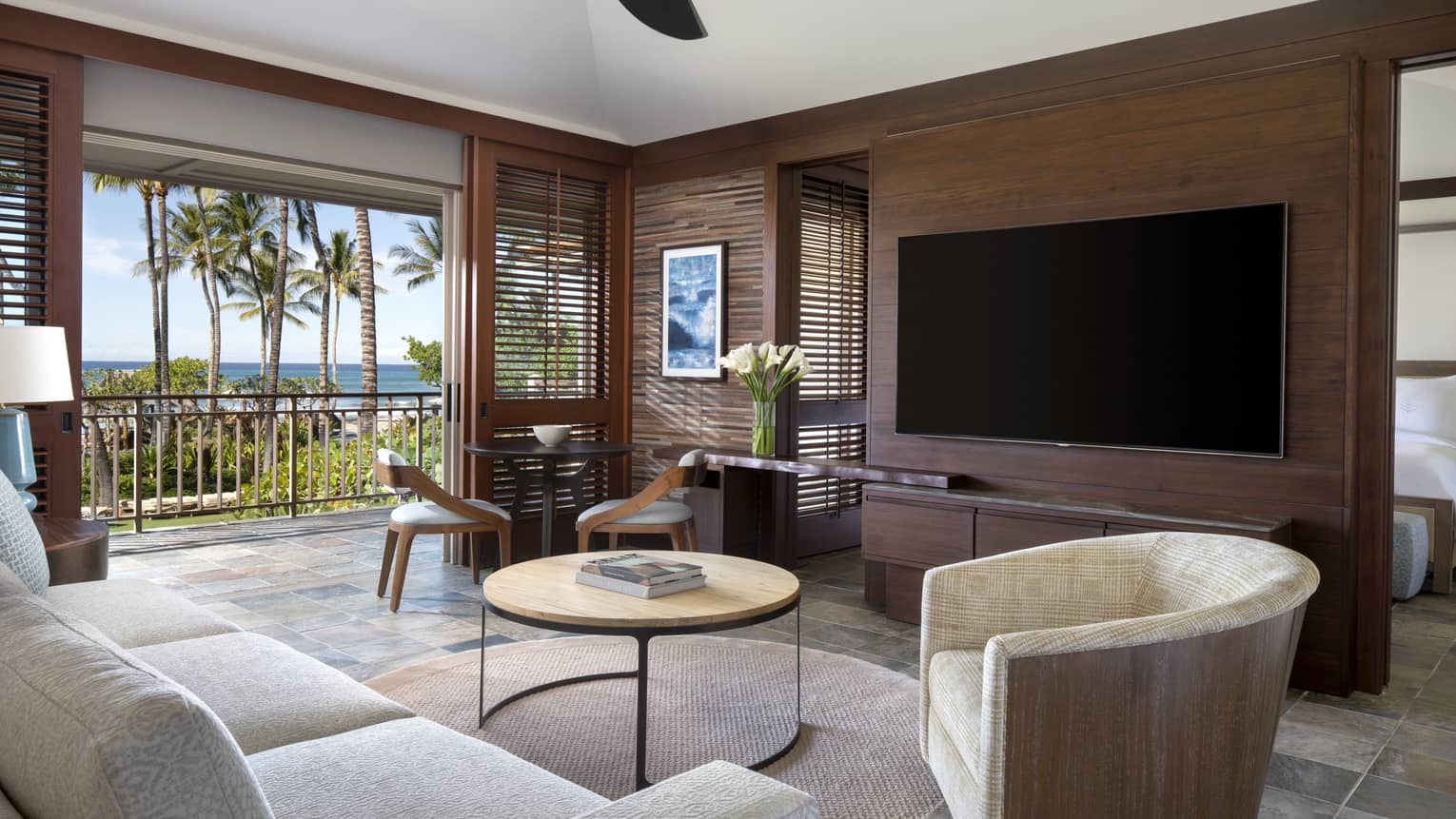 Living room with white sofa, tan arm chair, circular coffee table, wall-mounted TV, walk-out balcony