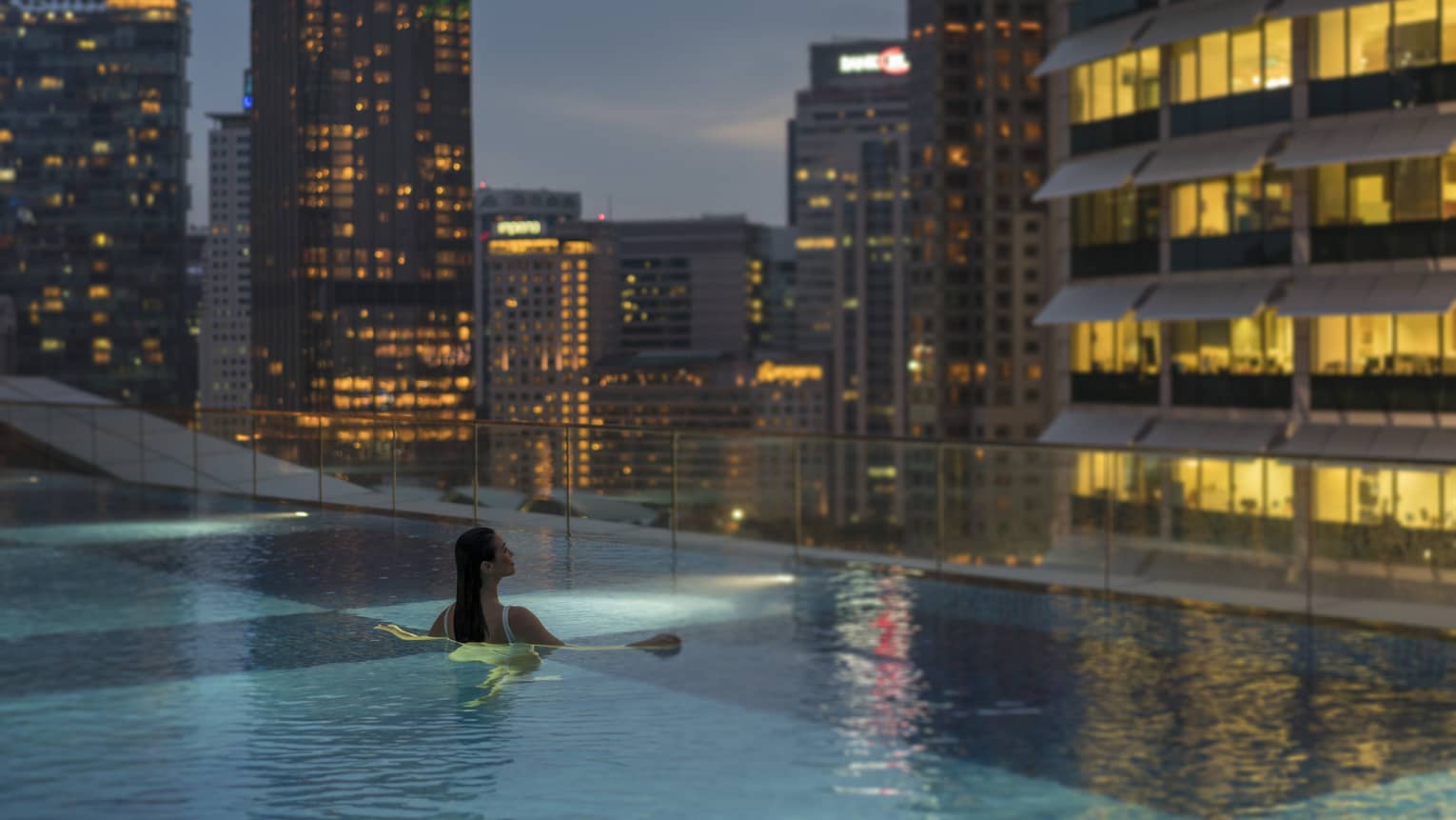 A woman swims in an infinity pool with a view of the city skyline