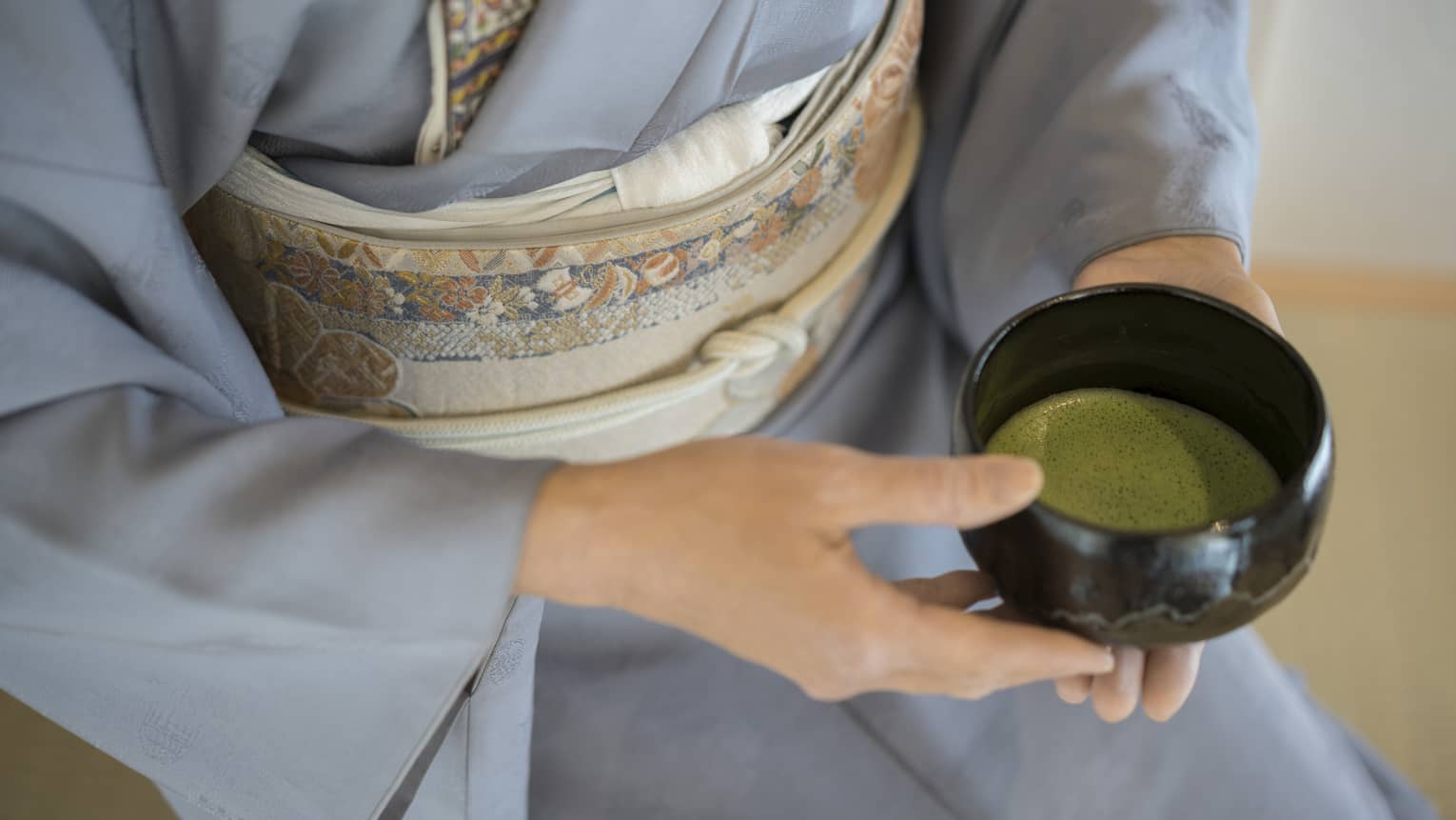 Close-up of woman in blue robe holding bowl with green matcha tea