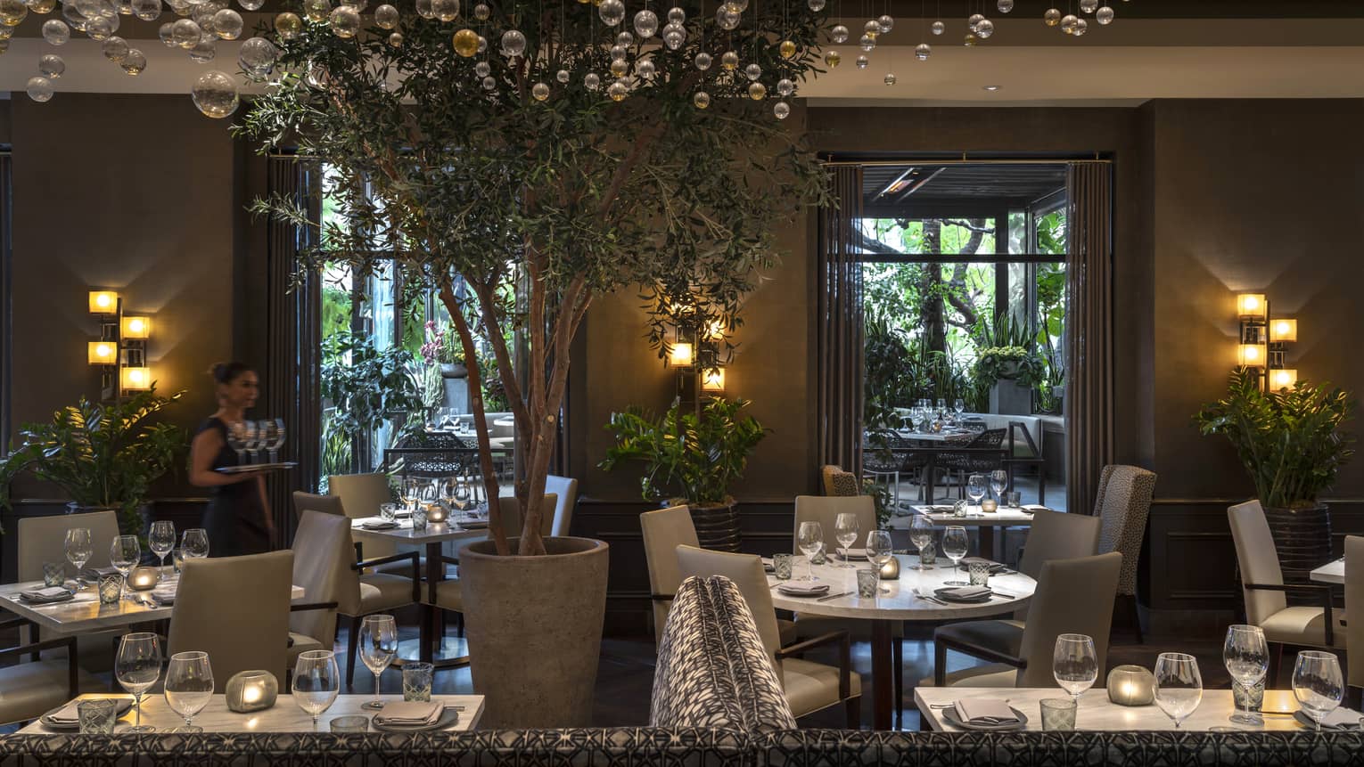 The interior of a dimly lit restaurant with white tables and grey chairs and bubble glass hanging like a chandelier.