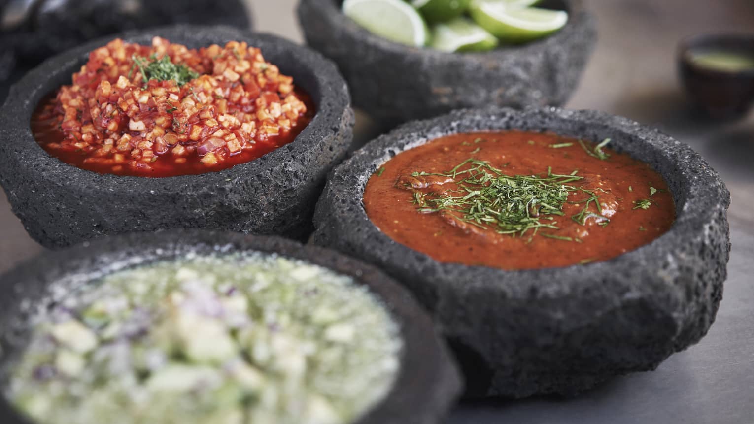 Four dark ceramic bowls contain sliced limes, salsa and pico de gallo 