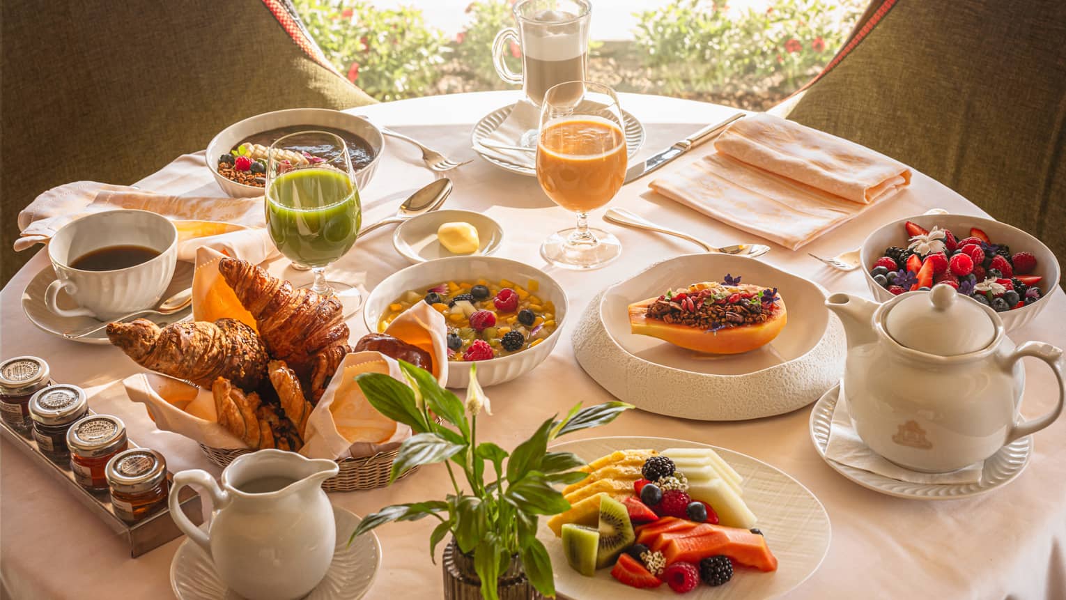 A round table in front of a window, set with an array of brunch dishes and beverages