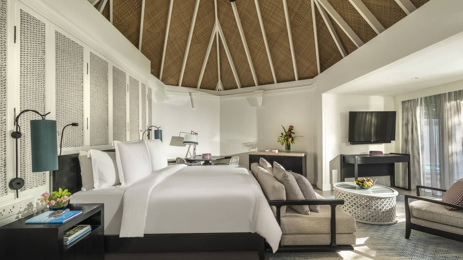 Beach pavilion bedroom with a king-size bed, vaulted thatched ceiling, cozy seating area and a flatscreen TV