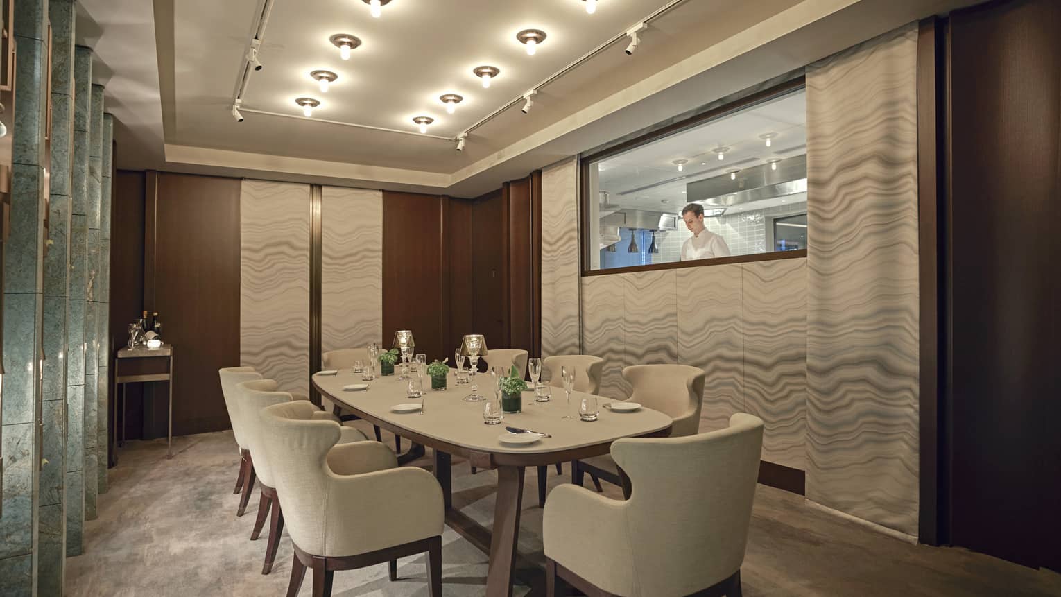 Private dining room with rectangular table and eight armchairs, low lighting, window to kitchen