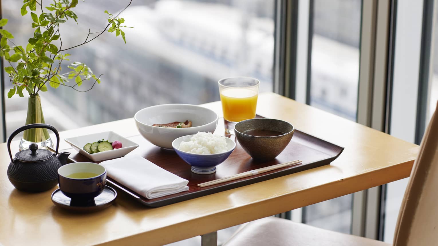 Japanese Breakfast on wooden tray with plant, window overlooking bullet trains