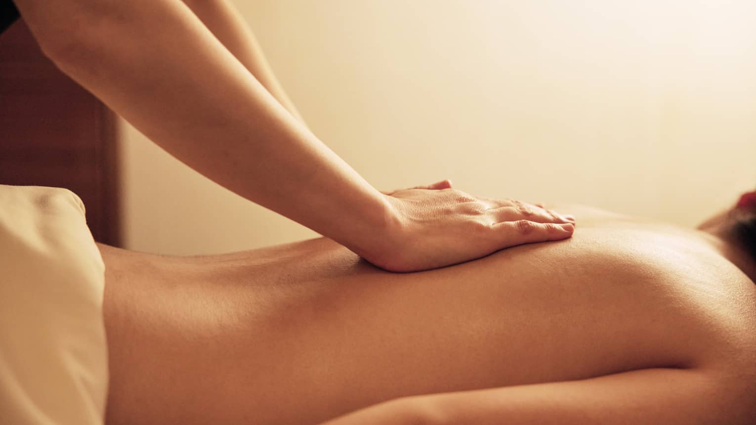Masseuse rests hands on woman's bare back as she lays on massage table