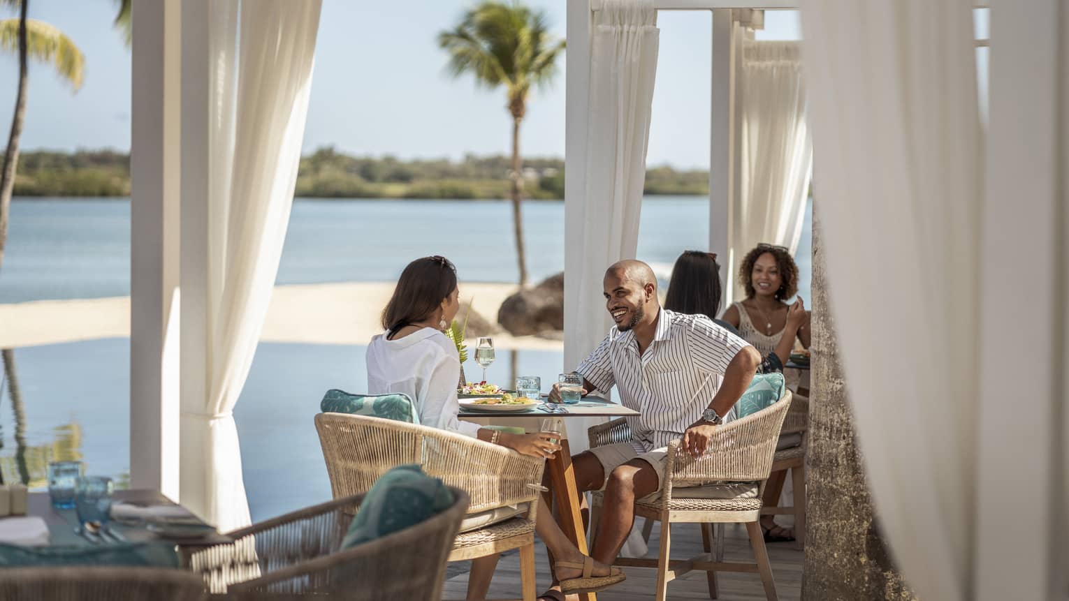 Couple sitting at waterfront restaurant, smiling over food and drinks 