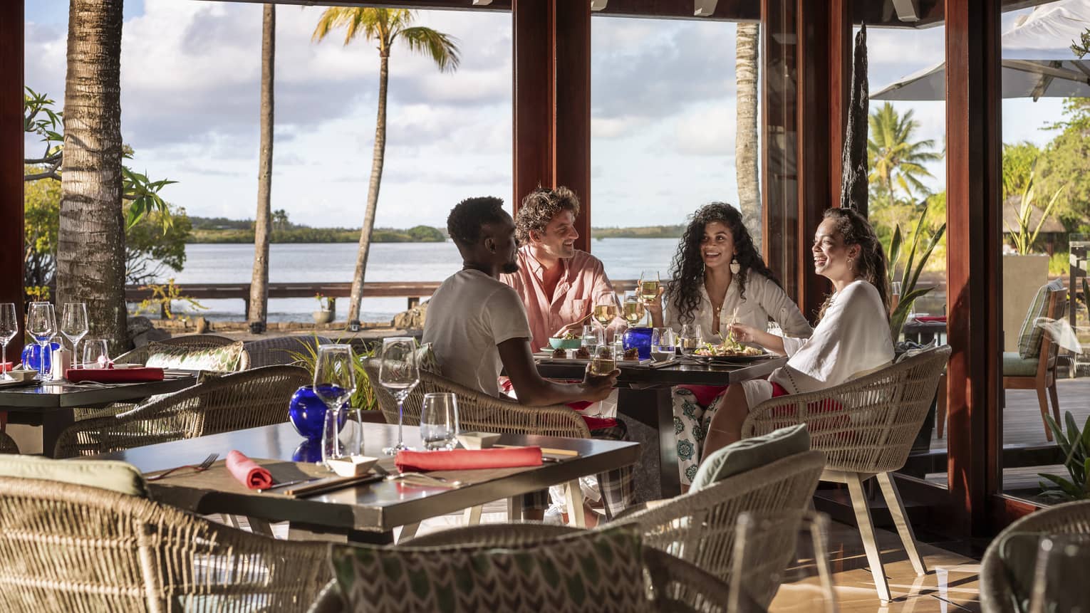 Four friends sitting and talking over food and wine at waterfront restaurant with tall windows