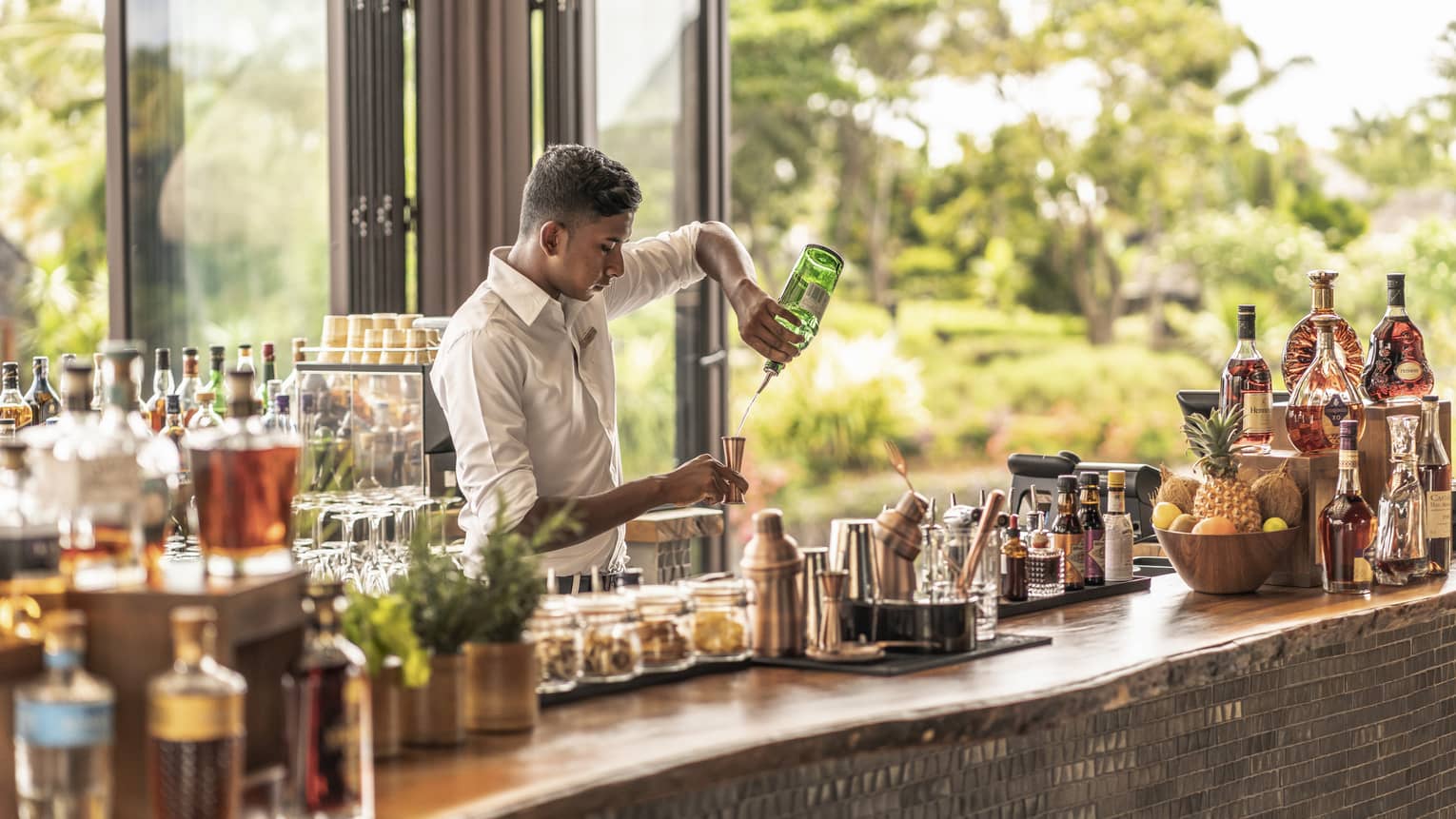 Bartender behind stocked bar pouring gin into a copper jigger