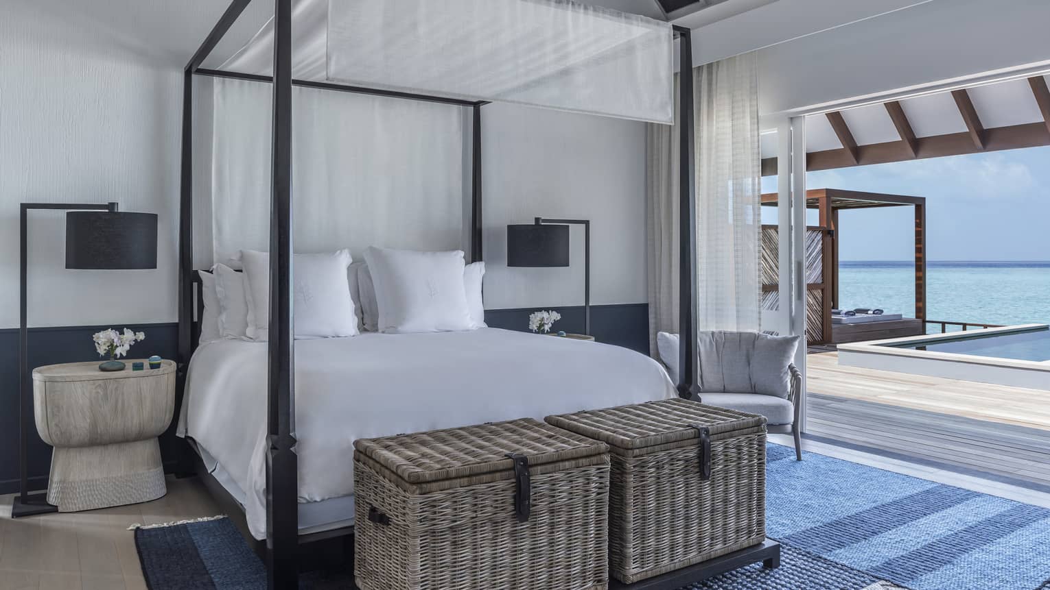 A four poster bed near a sliding door leading to an oceanside pool