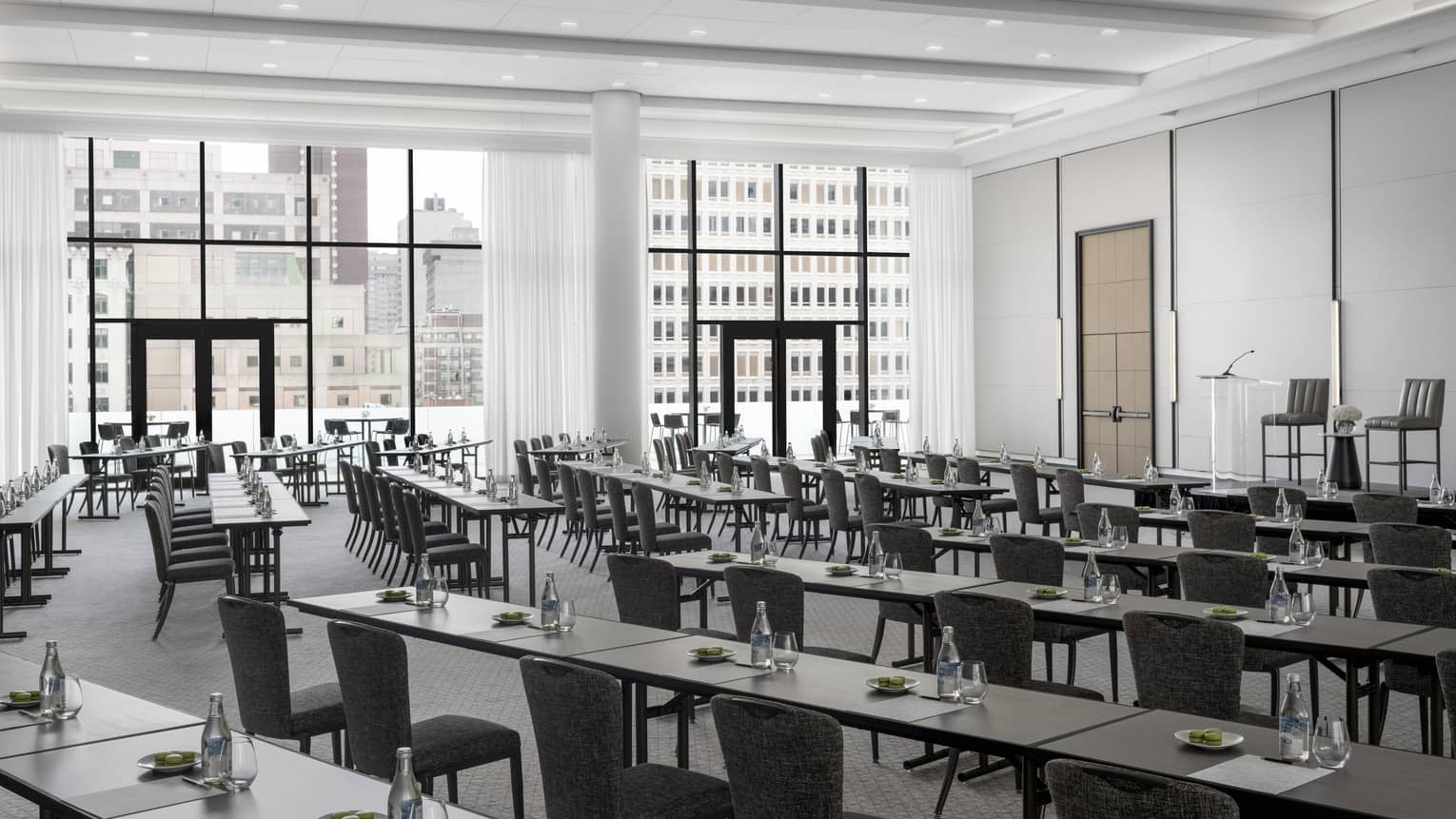 Rows of black tables set with green macaroons, water facing podium in light-filled ballroom