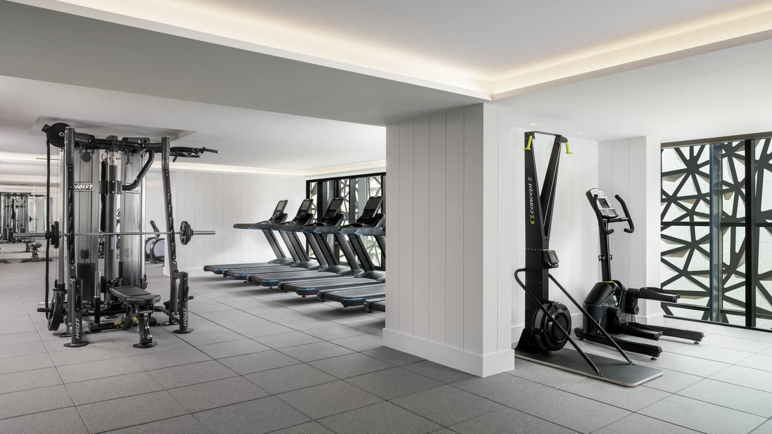 A large fitness space featuring a weights machine and several ellipticals. 