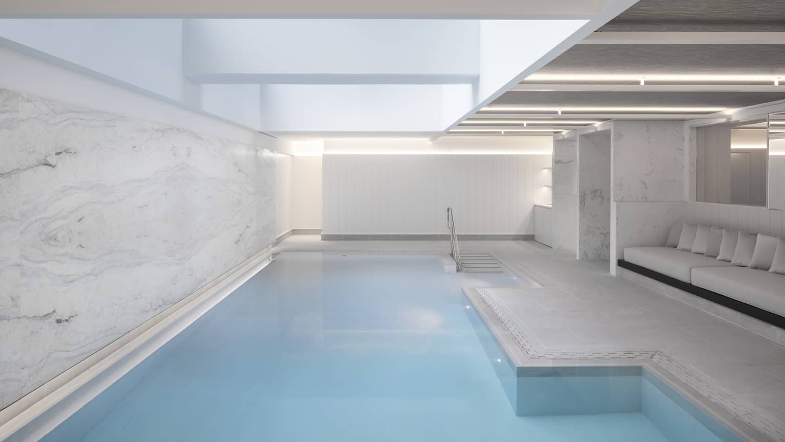 Indoor pool at spa, banquet of seating on one side, marbled wall on other 